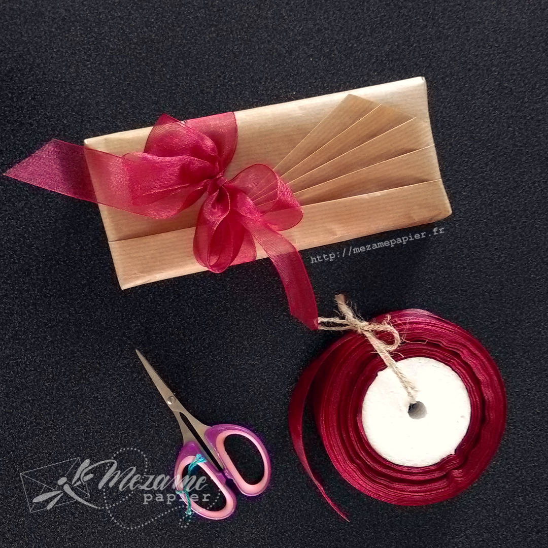 paquet cadeau allongé avec des plis en éventail selon techniques de l'école Shiho Masuda avec un grand nœud double en organza rouge bordeaux