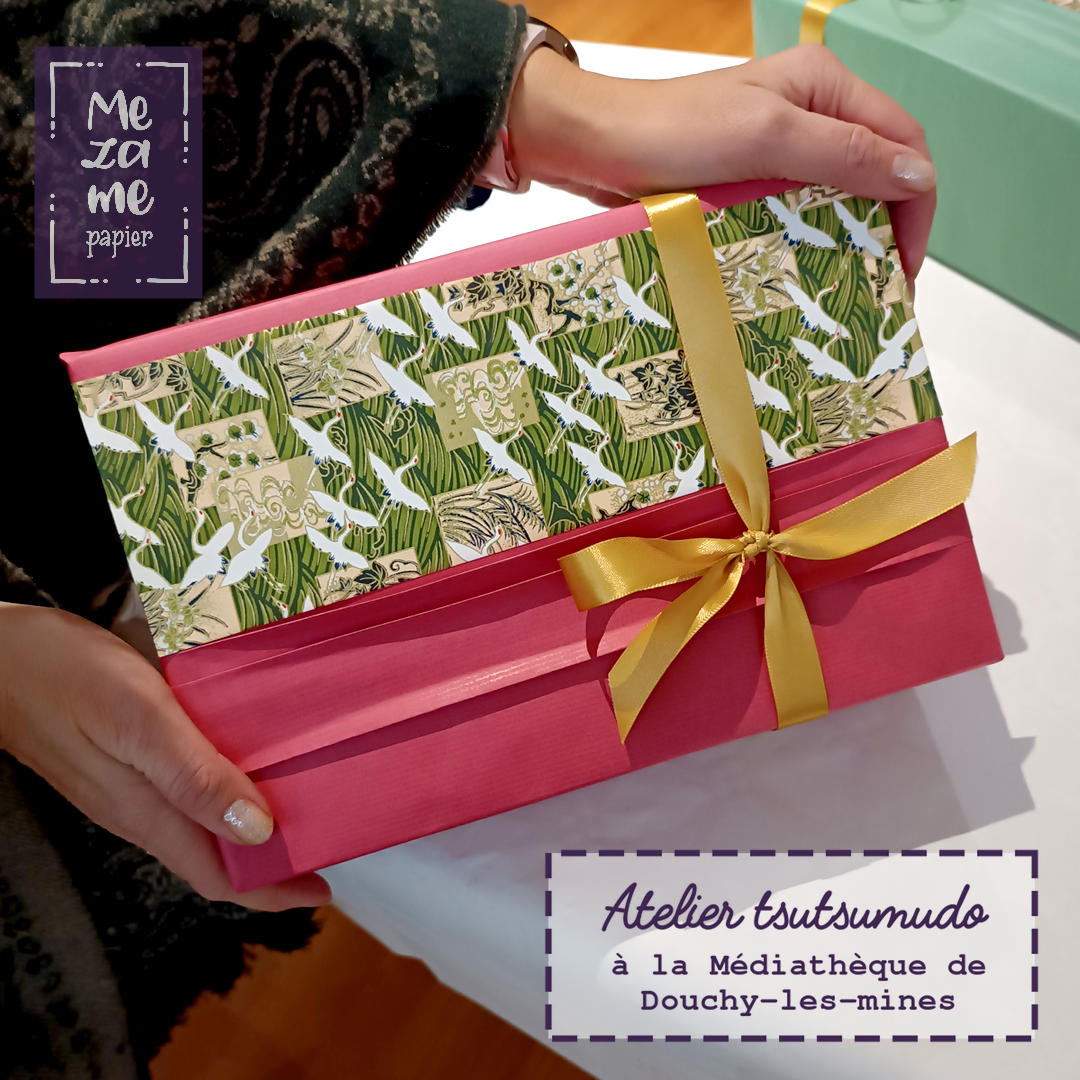 Cadeau emballé dans du papier kraft fushsia avec un accent de papier japonais vert sapin décoré de grue blanches et dorées