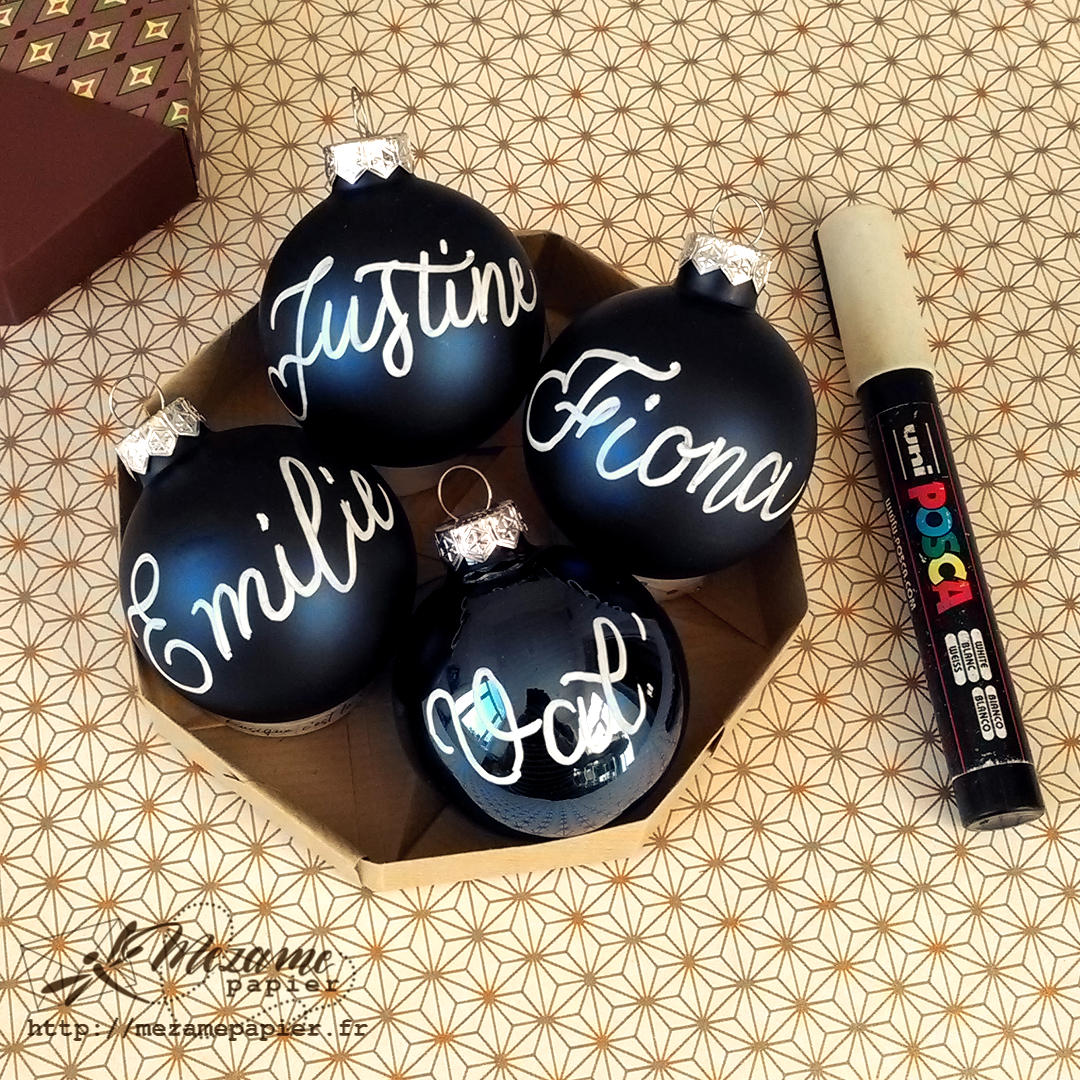 Boules de Noël couleur bleu nuit, avec personnalisation prénom à l'encre blanche, en calligraphie moderne, à l'intérieur d'une boîte poctogonale en origami