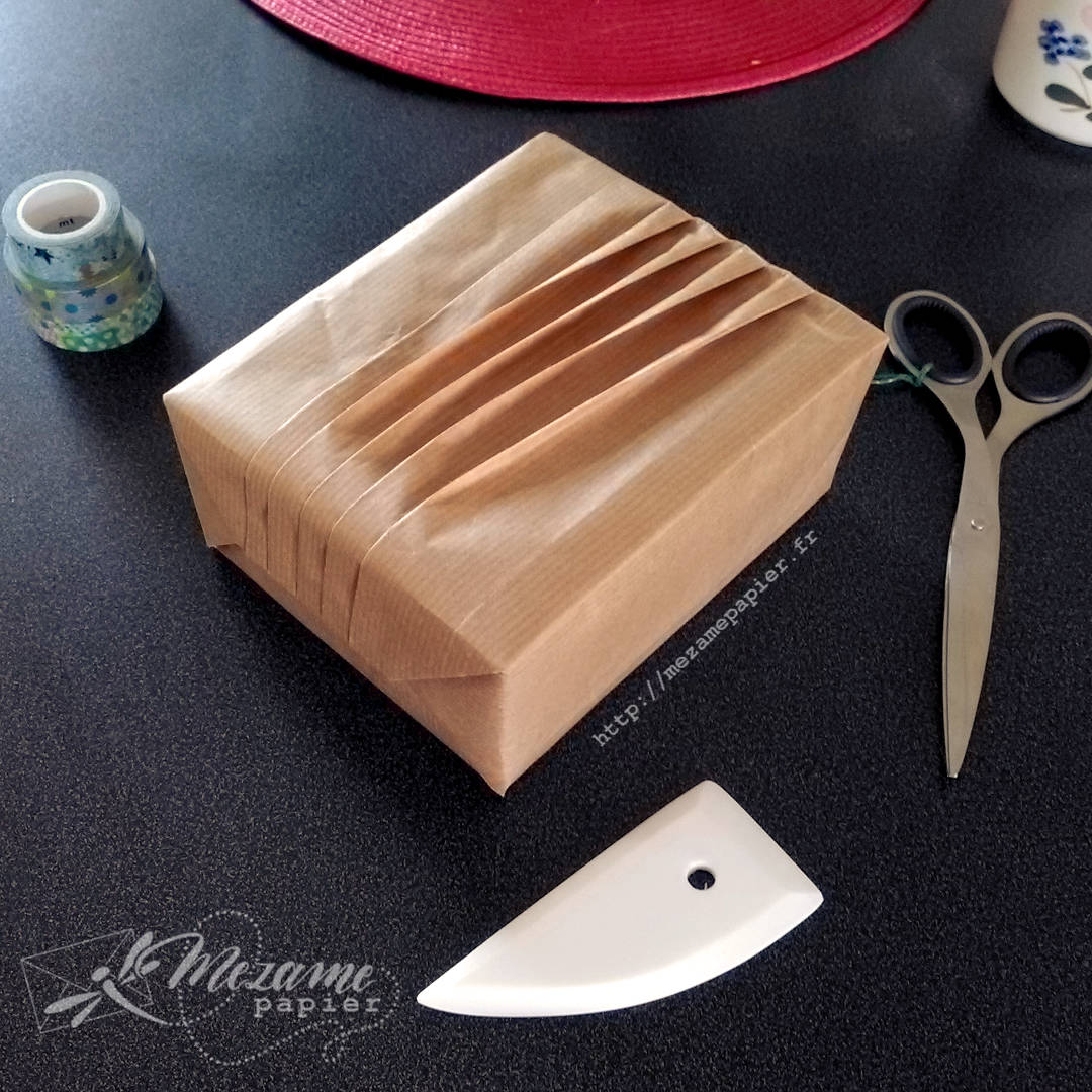 Paquet cadeau en kraft blond d'une boîte rectangulaire avec des plis qui tournicotent selon une technique de l'école Shiho Masuda