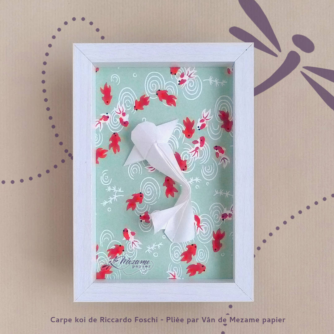 Cadre photo avec rebord blanc contenant une carpe origami et un lotus origami en papiers japonais nacré, sur fond de papier japonais turquoise au motif de fleurs de cerisiers